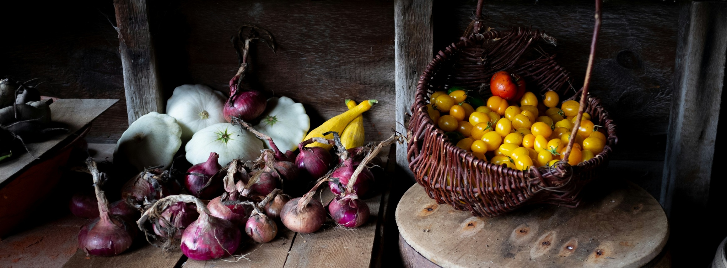 Rustic produce still life with garlic, onions, and yellow cherry tomatoes in a basket